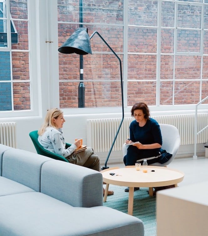 Two women sitting and chatting in an office setting.