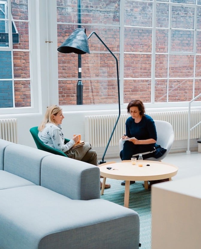 Two women sitting and talking in an office setting.