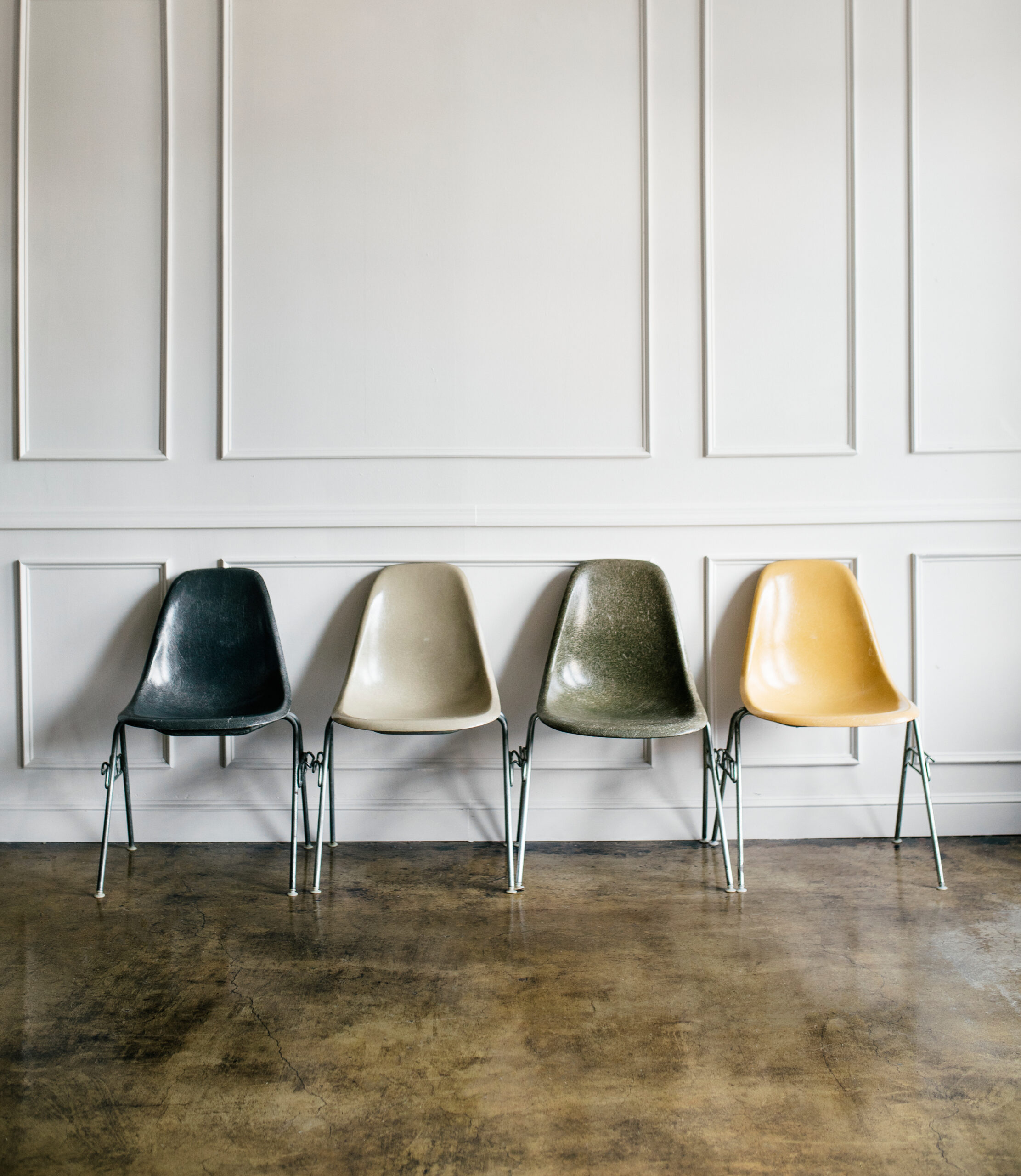 Pleasing artistic image of 4 chairs in neutral tones of charcoal, beige, army green, and subdued yellow.