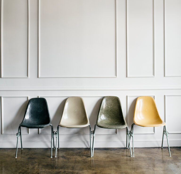 Pleasing artistic image of 4 chairs in neutral tones of charcoal, beige, army green, and subdued yellow.