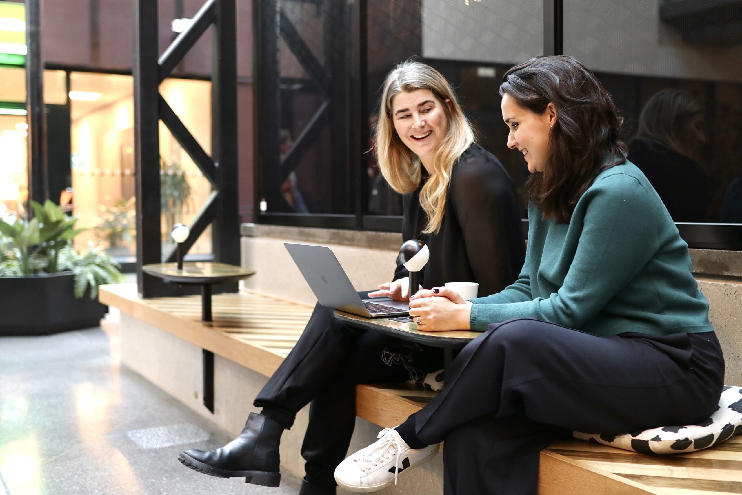 Photo of two Vaimo employees sitting and looking at a laptop together, laughing