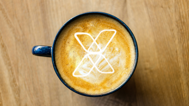 image of coffee cup on wooden table with Vaimo logo in the milk foam